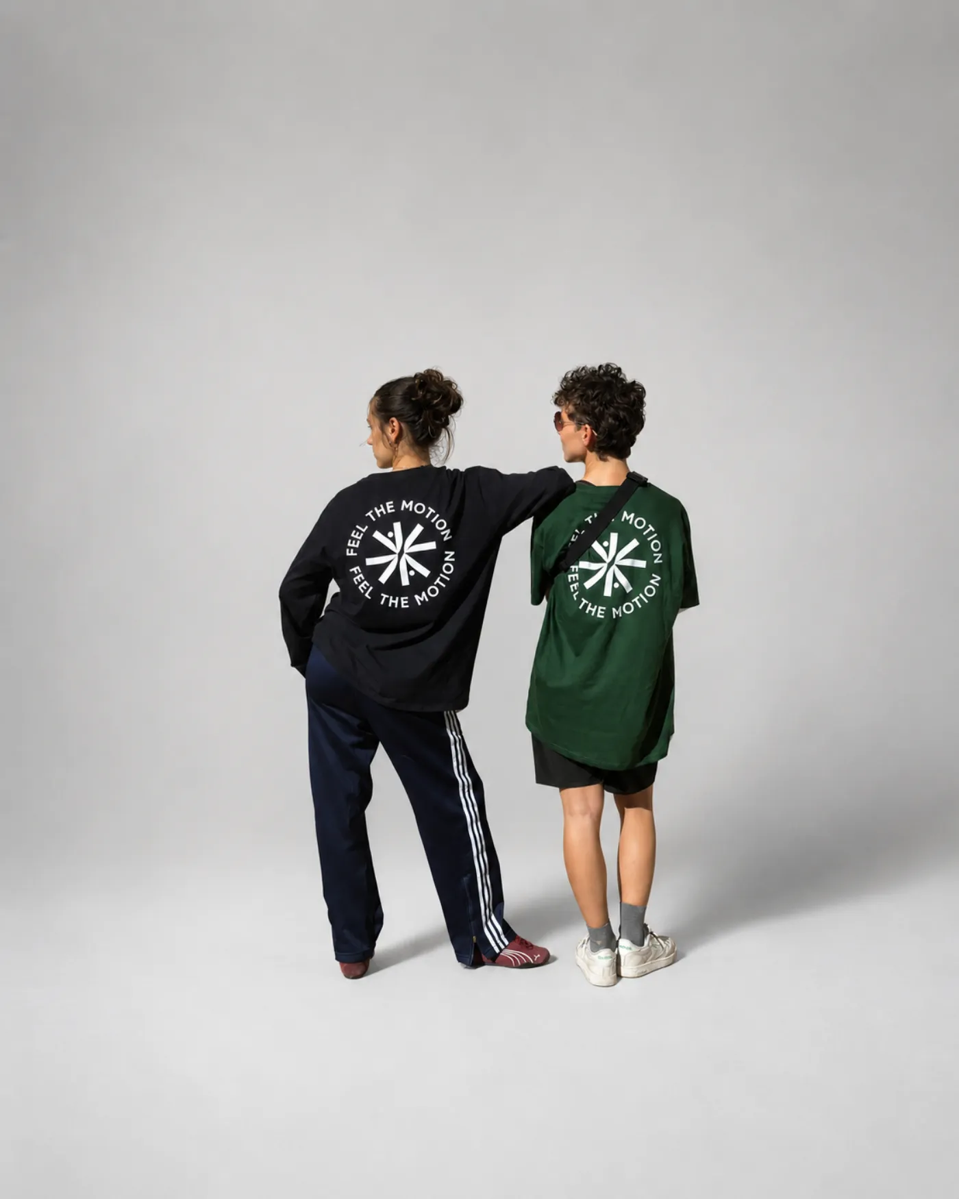 Deux personnes de dos portant le t-shirt manches longues noir et le t-shirt manches courtes vert bouteille, logo Feel The Motion imprimé dans le dos
